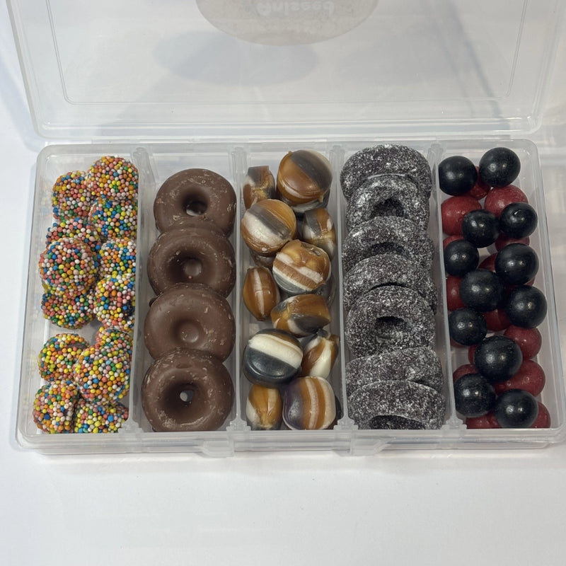 Snack box filled with assorted aniseed confectionery, including colourful aniseed sparkles, milk chocolate aniseed rings, striped humbugs, sugar-coated black aniseed rings and black and red aniseed balls.
