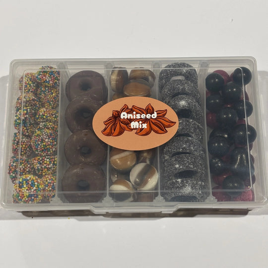 Clear five-compartment snack box filled with assorted aniseed confectionery, including colourful aniseed sparkles, milk chocolate aniseed rings, striped humbugs, sugar-coated black aniseed rings and black and red aniseed balls.