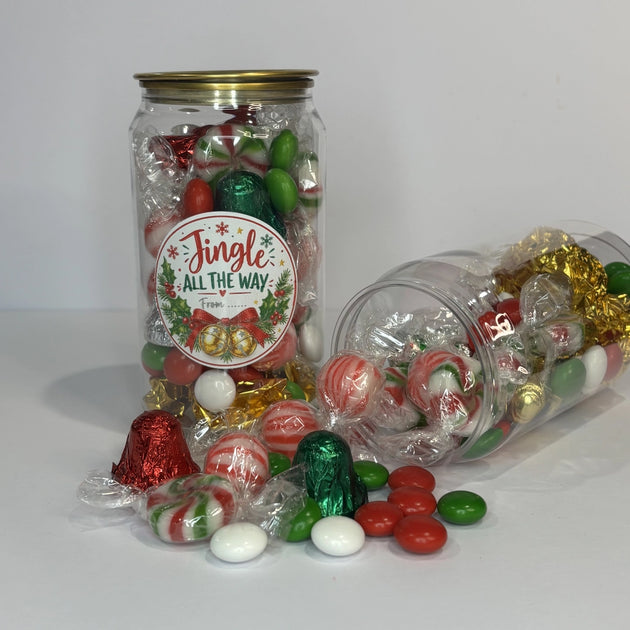 Christmas lolly cans filled with assorted festive confectionery, including striped mints, foil-wrapped chocolates and colourful chocolate buttons, with lollies spilling onto a white surface.