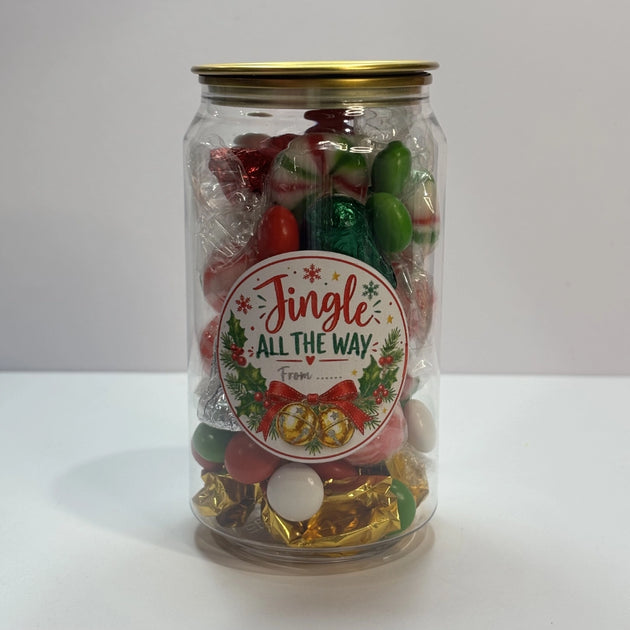 Clear Christmas lolly can with gold lid and festive “Jingle All the Way” label, filled with red, green and white lollies, wrapped mints and chocolates.