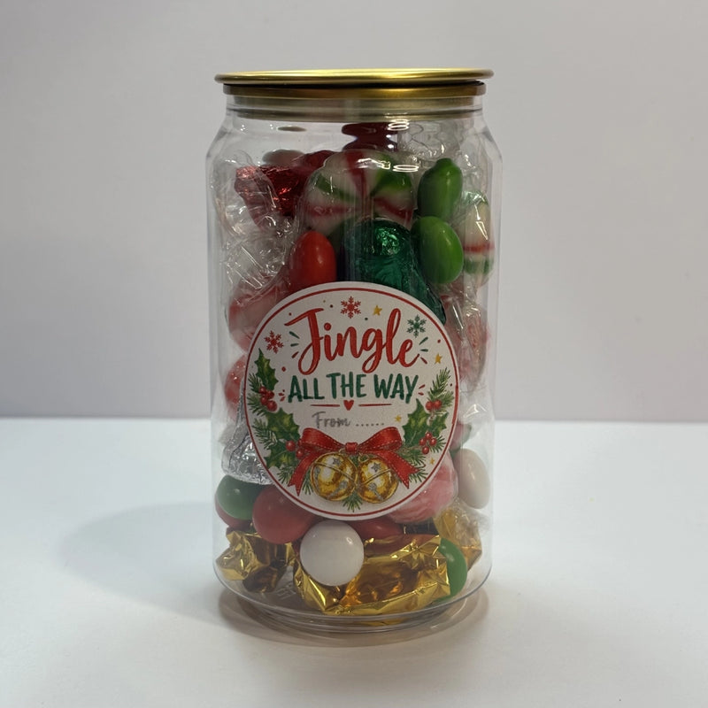 Clear Christmas lolly can with gold lid and festive “Jingle All the Way” label, filled with red, green and white lollies, wrapped mints and chocolates.