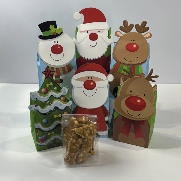Assorted Christmas gift bags featuring Santa, snowmen, reindeer and Christmas tree designs, with a clear bag of golden peanut brittle displayed in front.