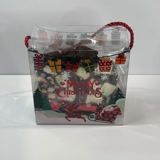 Clear Christmas gift bag with red rope handles and festive Merry Christmas decorations, containing a large 320g piece of rocky road with chocolate, marshmallows, nuts and jubes.