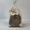 Clear gift bag filled with round milk chocolate Christmas speckles covered in red, green and white sprinkles, finished with a Merry Christmas tree-shaped gift tag.
