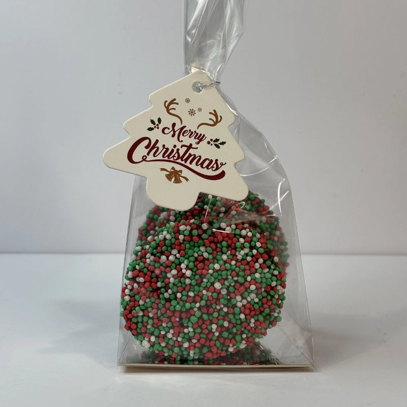 Clear gift bag filled with round milk chocolate Christmas speckles covered in red, green and white sprinkles, finished with a Merry Christmas tree-shaped gift tag.