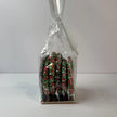 Side view of clear gift bag filled with round milk chocolate Christmas speckles covered in red, green and white sprinkles, finished with a Merry Christmas tree-shaped gift tag.