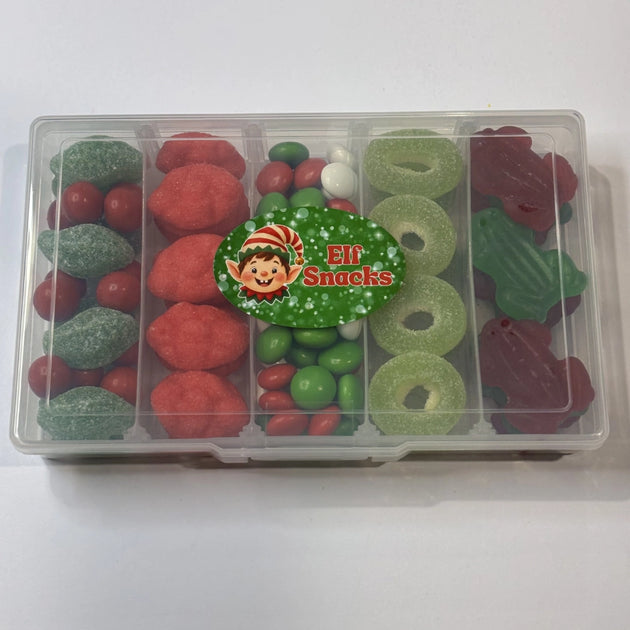 A clear plastic compartment box filled with assorted Christmas themed snack box filled with assorted red, green and white lollies and chocolates, including spearmint leaves, Jaffas, strawberry clouds, chocolate buttons, apple rings and frogs, with an Elf Snacks label on the lid.