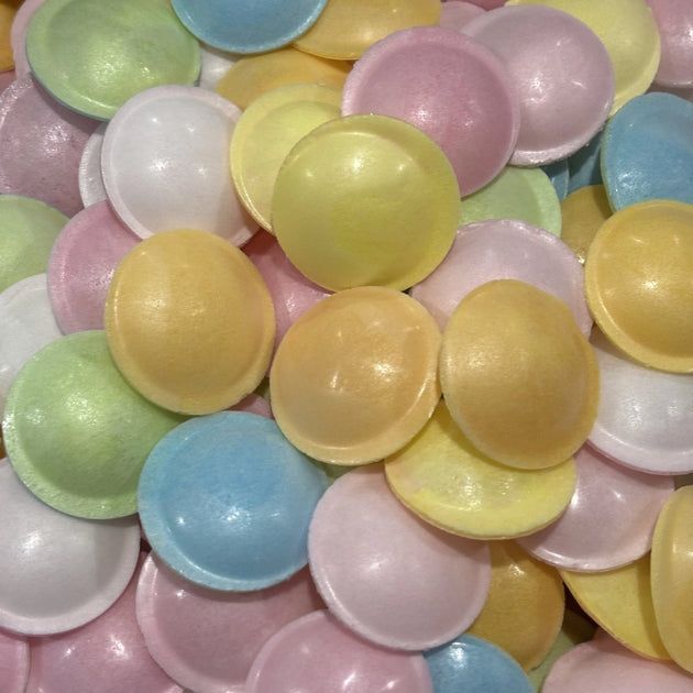 A close-up pile of small, disc-shaped wafers in pastel colors including yellow, pink, blue, green, and white.