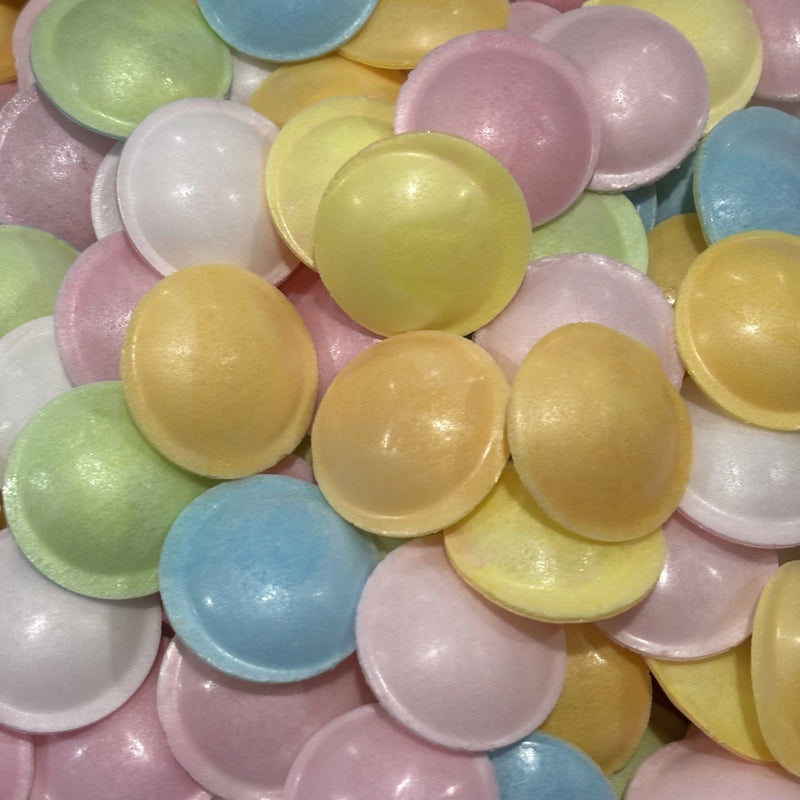 A close-up pile of small, disc-shaped wafers in pastel colors including yellow, pink, blue, green, and white.