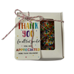 A square gift box filled with colorful chocolate freckles, tied with string and a gift tag that reads 'THANK YOU for all that you do! YOU ARE APPRECIATED MORE THAN YOU KNOW!'