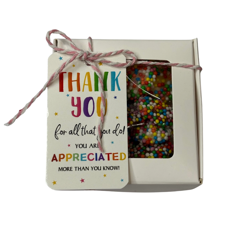 A square gift box filled with colorful chocolate freckles, tied with string and a gift tag that reads 'THANK YOU for all that you do! YOU ARE APPRECIATED MORE THAN YOU KNOW!'