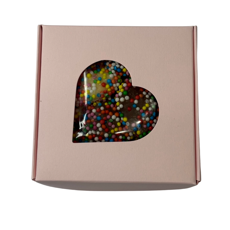 A square gift box with a heart-shaped clear window showing colorful chocolate freckles inside.