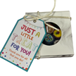 A square gift box tied with string and featuring a colorful printed tag that reads 'JUST A LITTLE TREAT FOR YOU!'. A round window on the box reveals fruit rock candy inside.