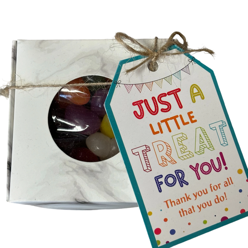 A square gift box with a circular window showing colourful jelly beans inside, tied with string and a gift tag that reads 'JUST A LITTLE TREAT FOR FOR YOU!'