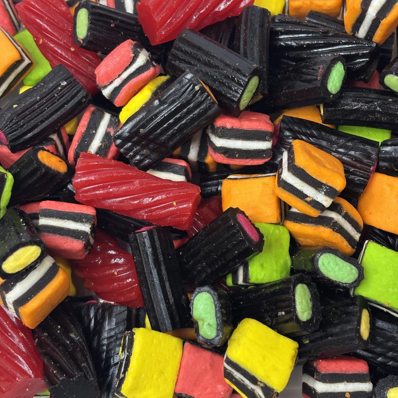 Close-up of assorted licorice allsorts featuring colourful pink, orange, yellow and green layers, black licorice pieces and red licorice twists.