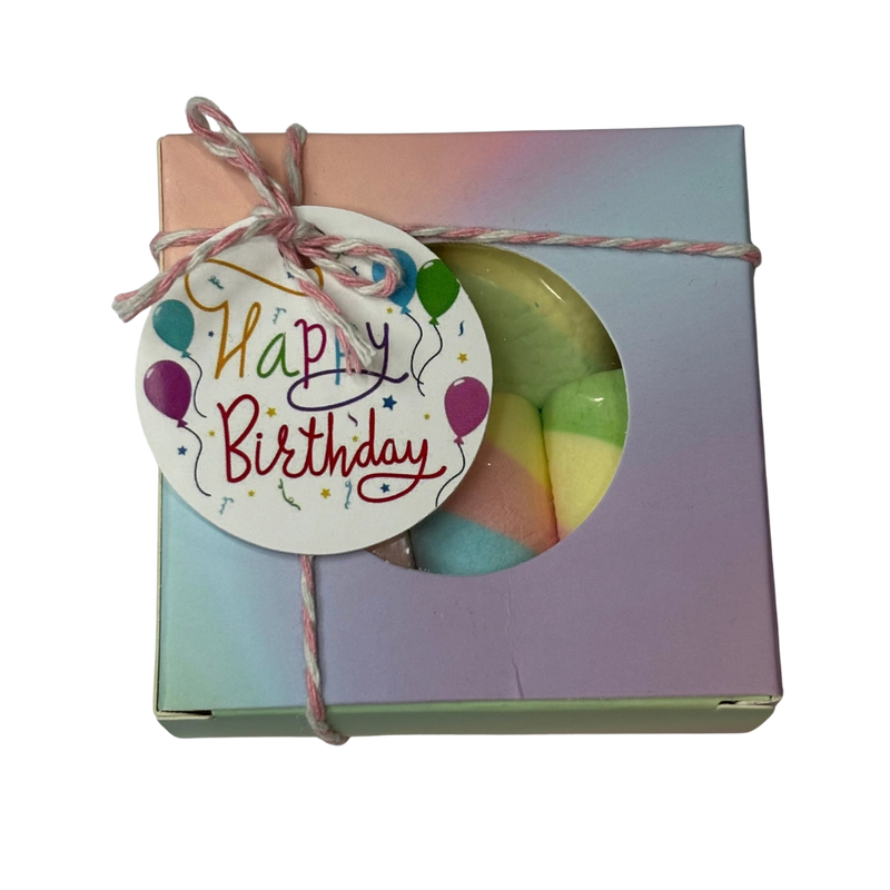 A square gift box with a circular window showing rainbow marshmallows, tied with string and a 'Happy Birthday' gift tag.