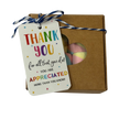 A square gift box with a heart-shaped window showing rainbow marshmallows inside, tied with string and a thank-you gift tag that reads 'THANK YOU for all that you do! YOU ARE APPRECIATED MORE THAN YOU KNOW!'