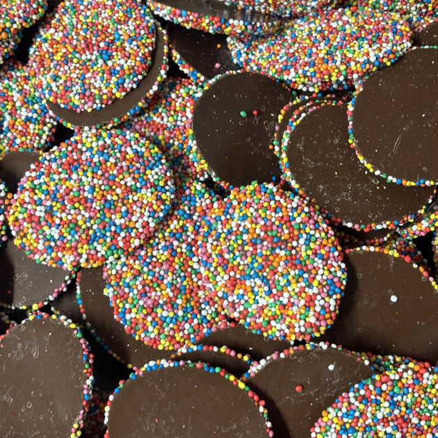 A pile of dark brown chocolate discs covered in multicolored round sprinkles.
