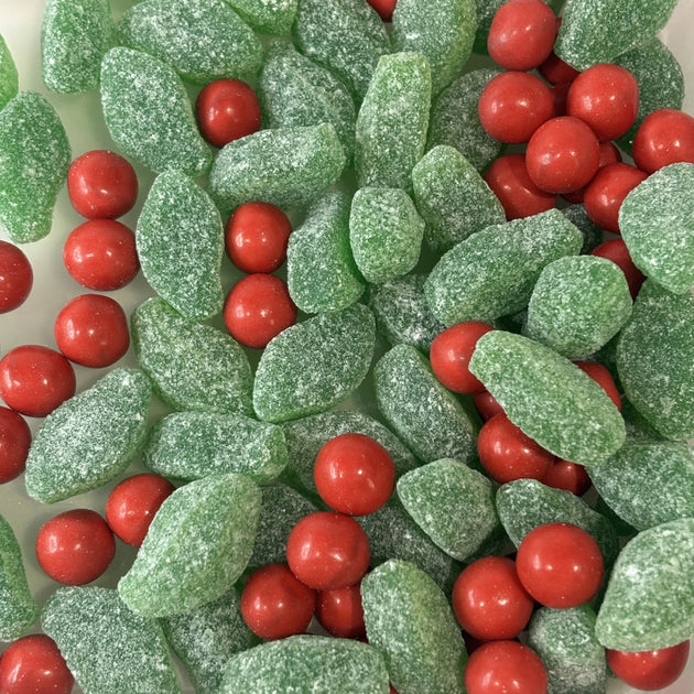Close-up of a festive lolly mix featuring green sugar-coated spearmint leaves and red candy-coated chocolate orange balls (Jaffas).