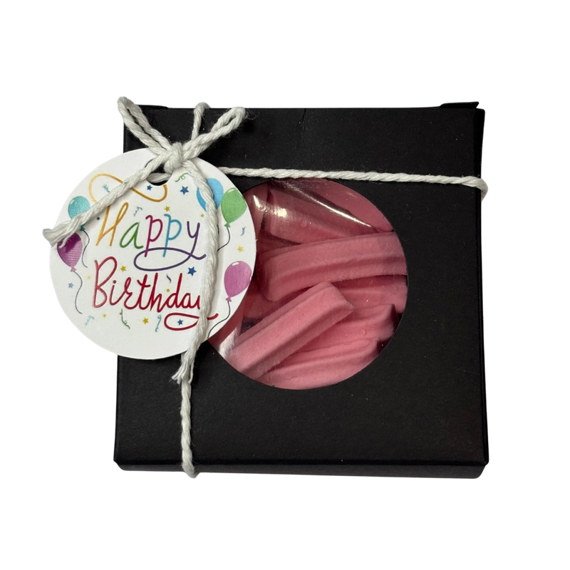 A gift box wrapped with twine and a 'Happy Birthday' gift tag, featuring a clear circular window that reveals pink mini musk sticks inside.
