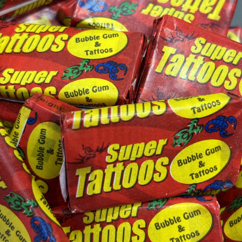 A close-up pile of red candy wrappers with bold yellow text reading 'Super Tattoos' and 'Bubble Gum & Tattoos'.