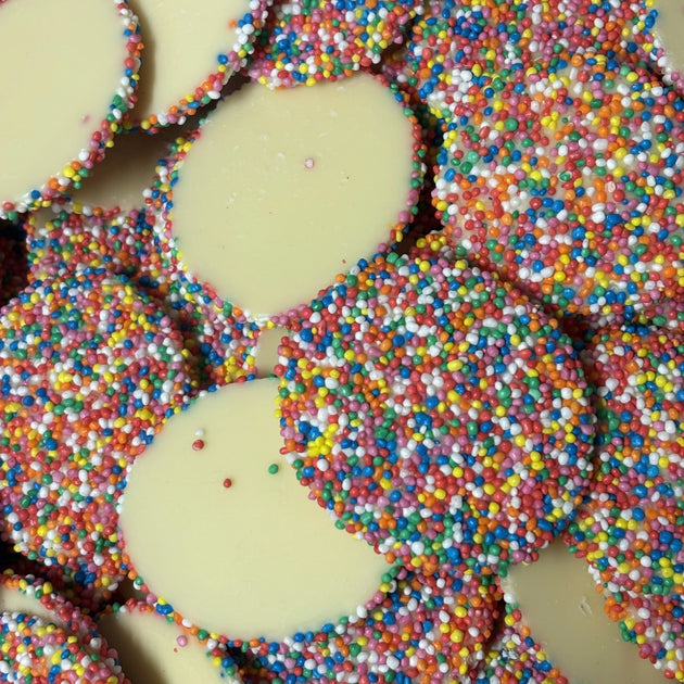 A pile of white chocolate discs covered in multicolored round sprinkles.